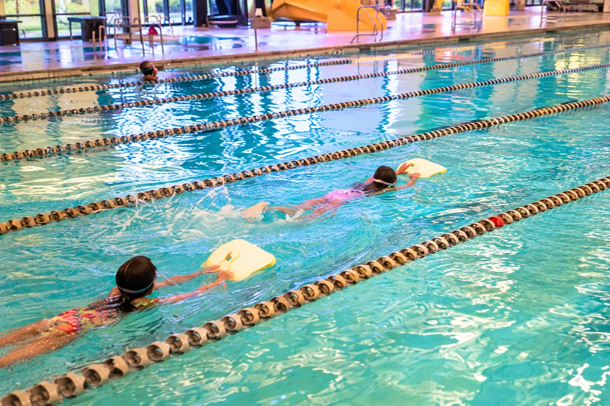 Older children actively swimming together in pool lanes with kickboards